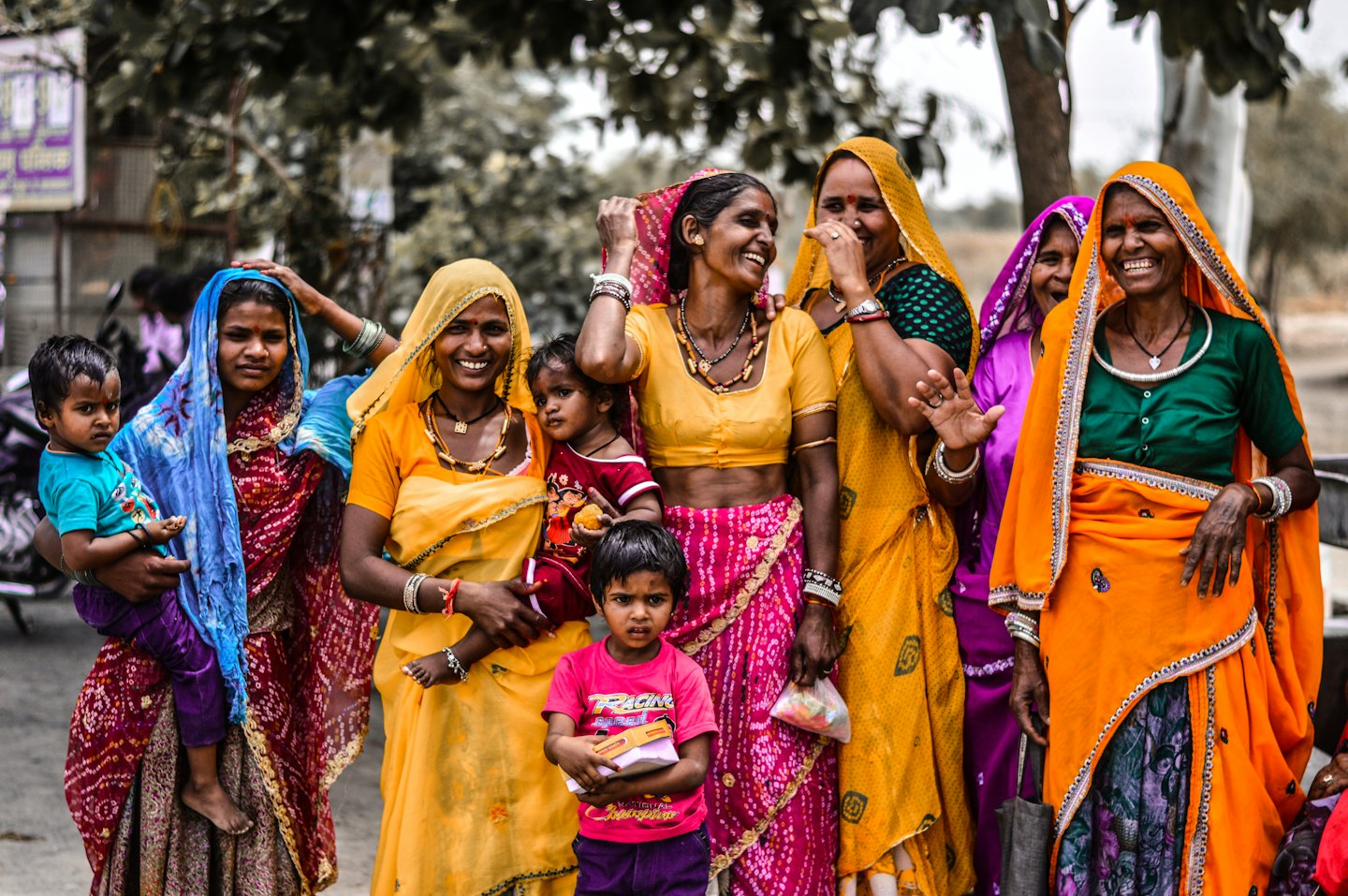 Smiling women and children in colorful traditional clothing outdoors.